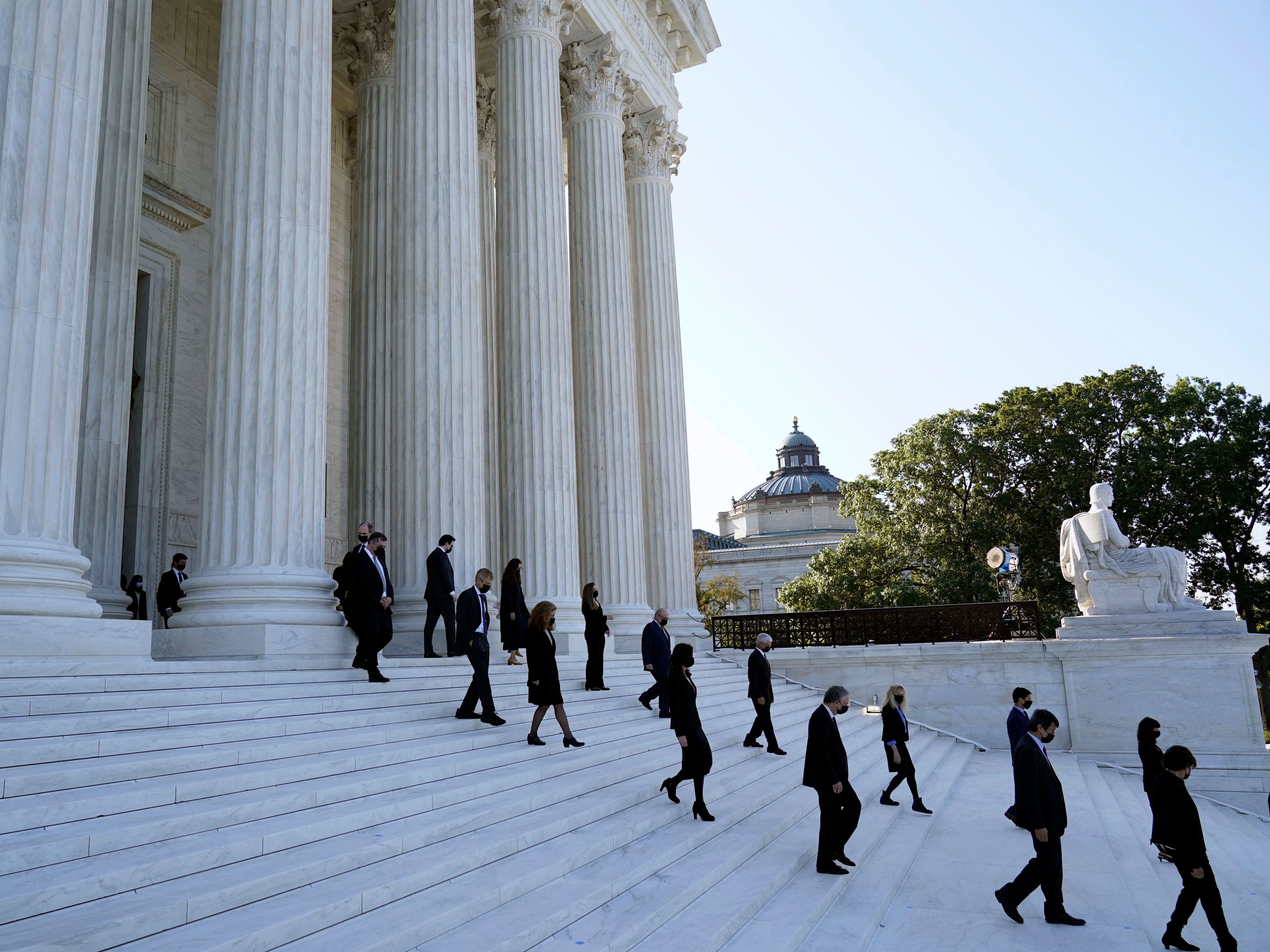 caption: Former law clerks for Justice Ruth Bader Ginsburg stand on the steps of the Supreme Court as they await the arrival of the casket of Ginsburg on Wednesday.