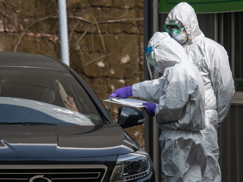 caption: Health workers in protective suits talk to a motorist at a drive-through testing center for COVID-19 in Seoul.