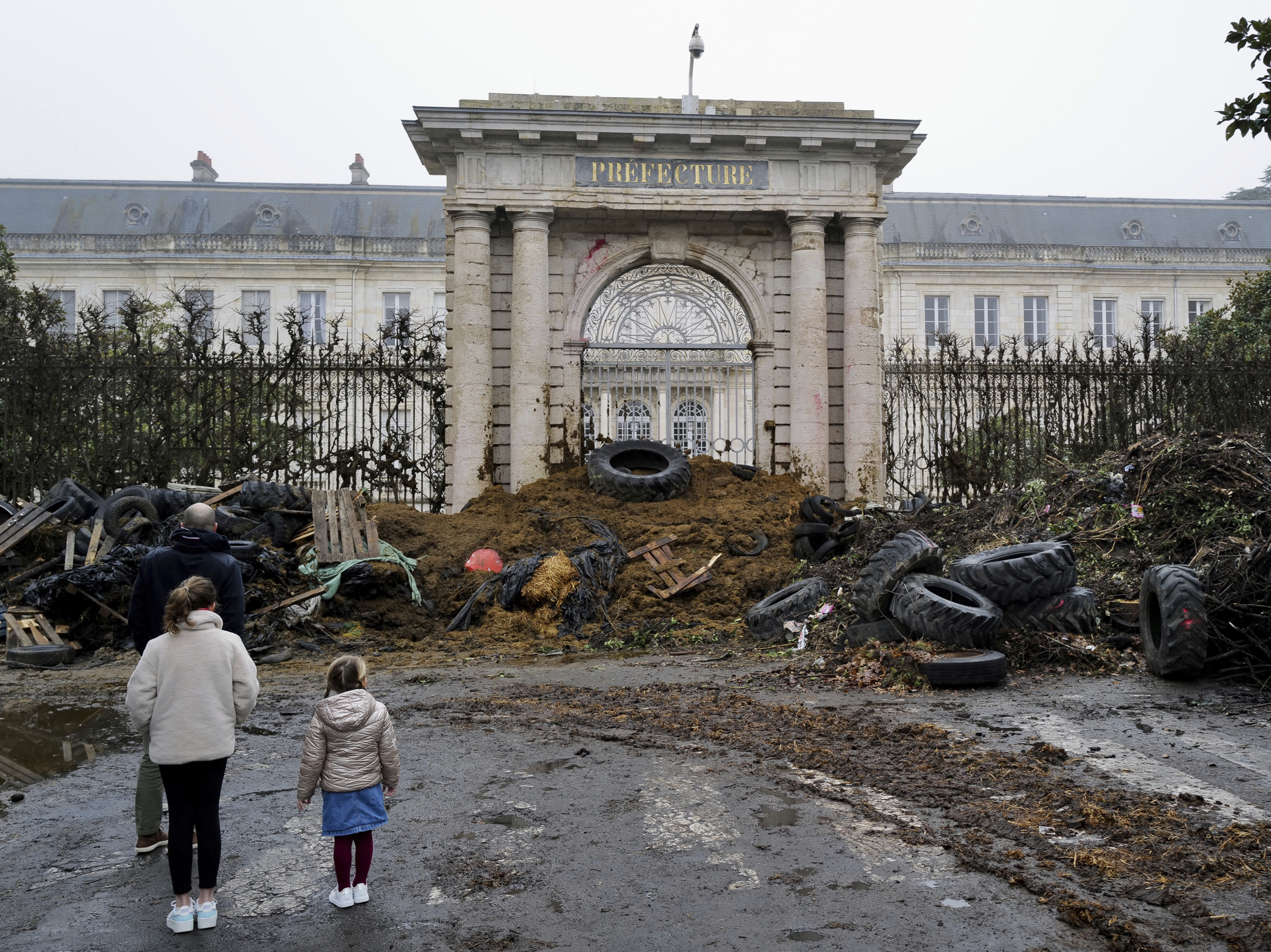 caption: People watch slurry, manure and tyres dumped by farmers at the entrance of the local state administration building, in Agen, southwestern France, Saturday, Jan. 27, 2024. French farmers have vowed to continue protesting and are maintaining traffic barricades on some of the country's major roads.