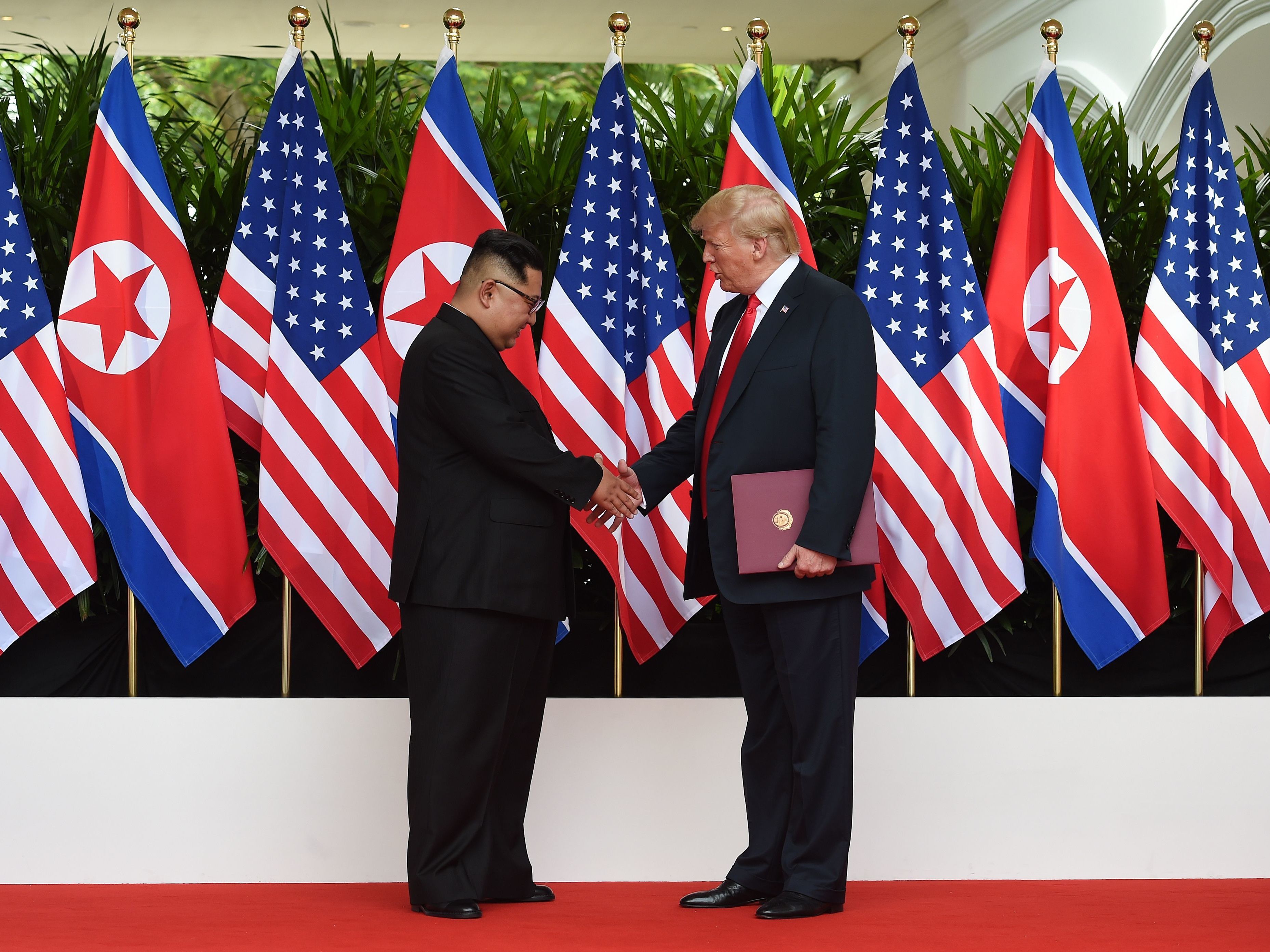 caption: North Korea's leader Kim Jong Un shakes hands with President Donald Trump after taking part in a signing ceremony at the end of their historic U.S.-North Korea summit, at the Capella Hotel on Sentosa island in Singapore on June 12, 2018.