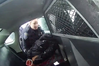 caption: A frame from a Rochester Police bodycam video showing a girl in handcuffs in the back of a police cruiser.