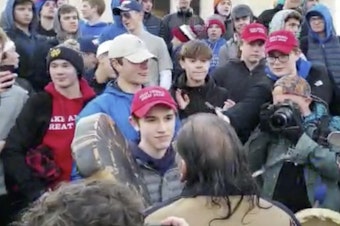 caption: A student wearing a "Make America Great Again" hat stands in front of a Native American singing and playing a drum in Washington on Friday. Young men and women surrounded Nathan Phillips, and a video of the incident has drawn outrage.