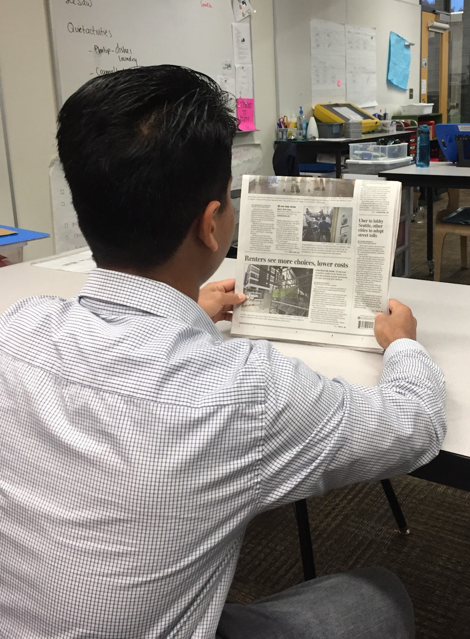 caption: Mohamad Imran reads the newspaper in classroom on Mercer Island.