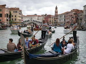 caption: Tourists enjoy a gondola ride on the Grand Canal by the Rialto bridge in Venice in 2021.