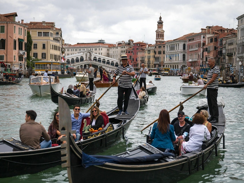 caption: Tourists enjoy a gondola ride on the Grand Canal by the Rialto bridge in Venice in 2021.