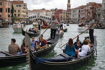 caption: Tourists enjoy a gondola ride on the Grand Canal by the Rialto bridge in Venice in 2021.