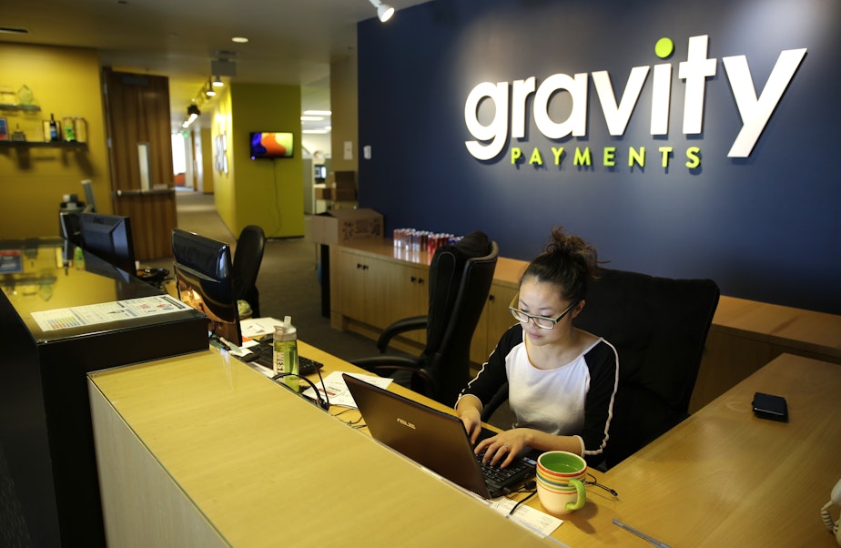caption: Cary Chin works at the front desk of Seattle-based Gravity Payments. CEO Dan Price told his employees earlier this year that he was cutting his own salary and using company profits so they would each earn a base salary of $70,000.