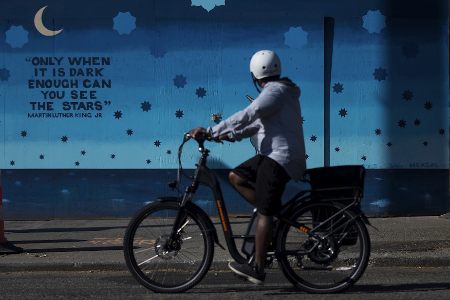 caption: A cyclist looks toward a mural painted by Scott McCall, covering the boarded up facade of Pho Big Bowl, along NW Market Street on Monday, April 20, 2020, in Seattle. The quote from Martin Luther King Jr. reads, "only when it is dark enough can you see the stars." 