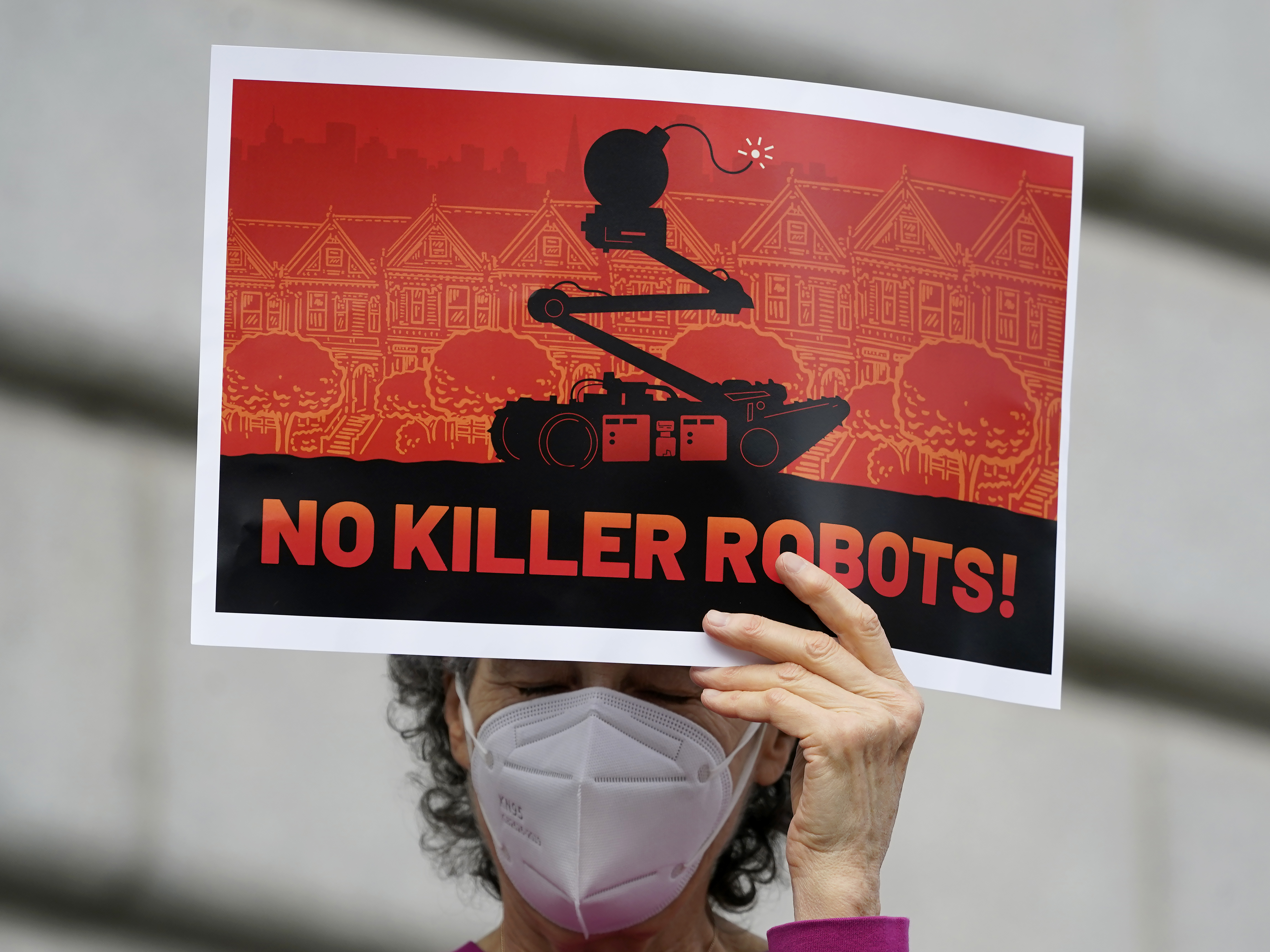 caption: A woman holds up a sign while taking part in a demonstration about the use of robots by the San Francisco Police Department outside of City Hall in San Francisco on Monday.
