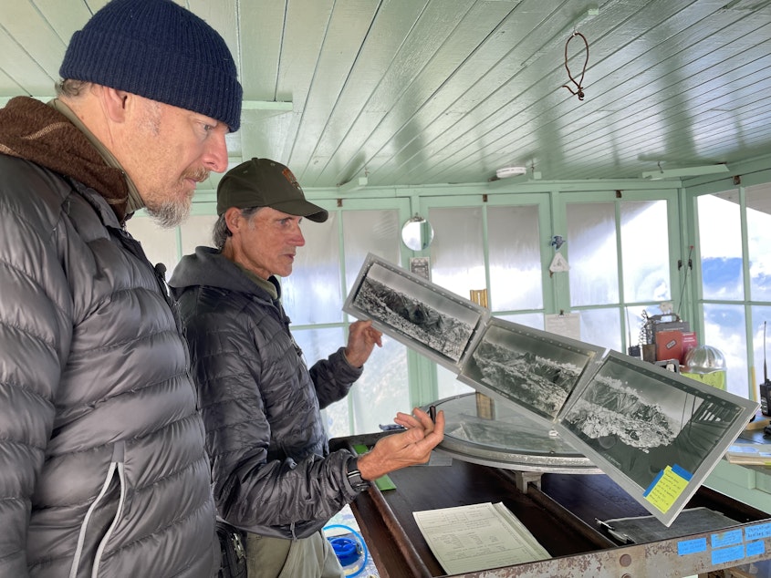 caption: Chris Morgan (left) and Jim Henterly (right) look at a photo of the mountain range taken from this lookout in 1933. 
