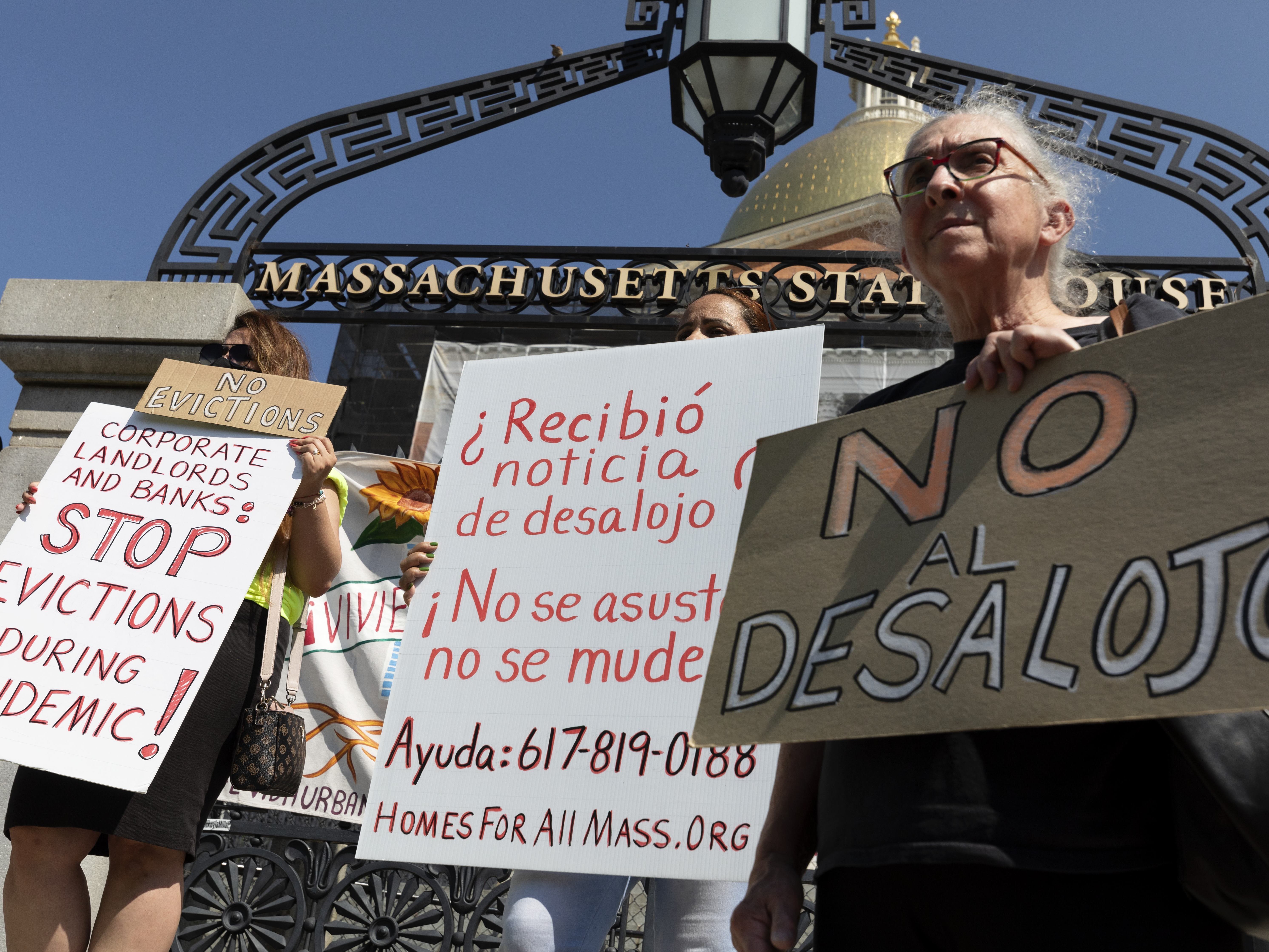 caption: People from a coalition of housing justice groups hold signs protesting evictions during a news conference outside the Statehouse on Friday in Boston.