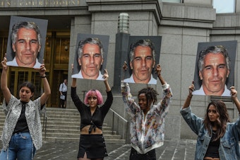 caption: A protest group called "Hot Mess" holds up signs of Jeffrey Epstein on July 8, 2019 in New York City.