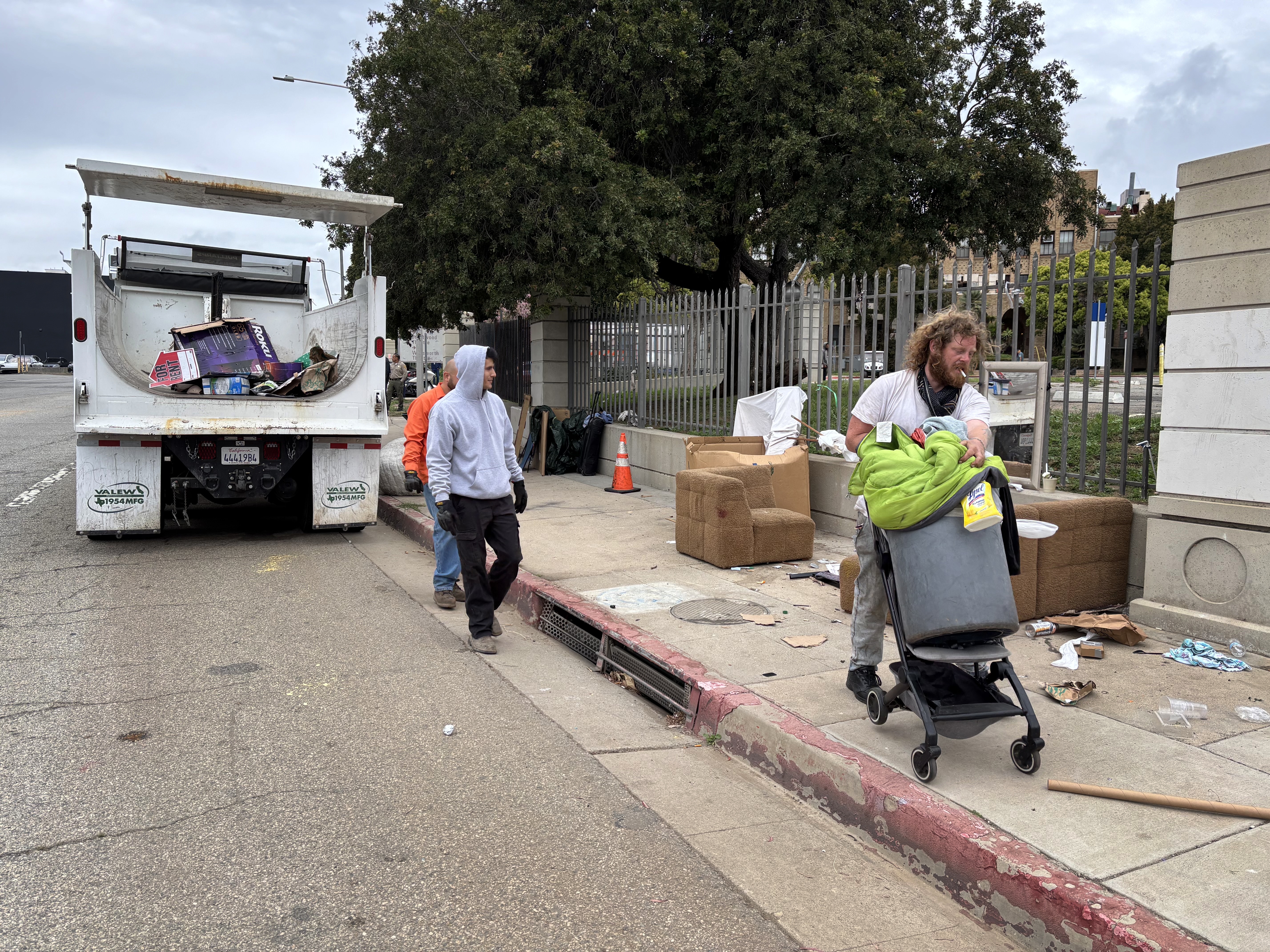 caption: Iraq war veteran Irving Webb moves his belongings as sanitation workers clear the sidewalk, where he spent some nights in April, outside the Los Angeles VA campus.