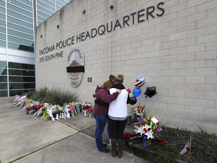 caption: Three women embrace as they stand at a growing memorial, Thursday, Dec. 1, 2016, at Tacoma Police Department headquarters in Tacoma, Wash. A Tacoma Police officer died Wednesday night at a hospital after being shot multiple times earlier in the day.