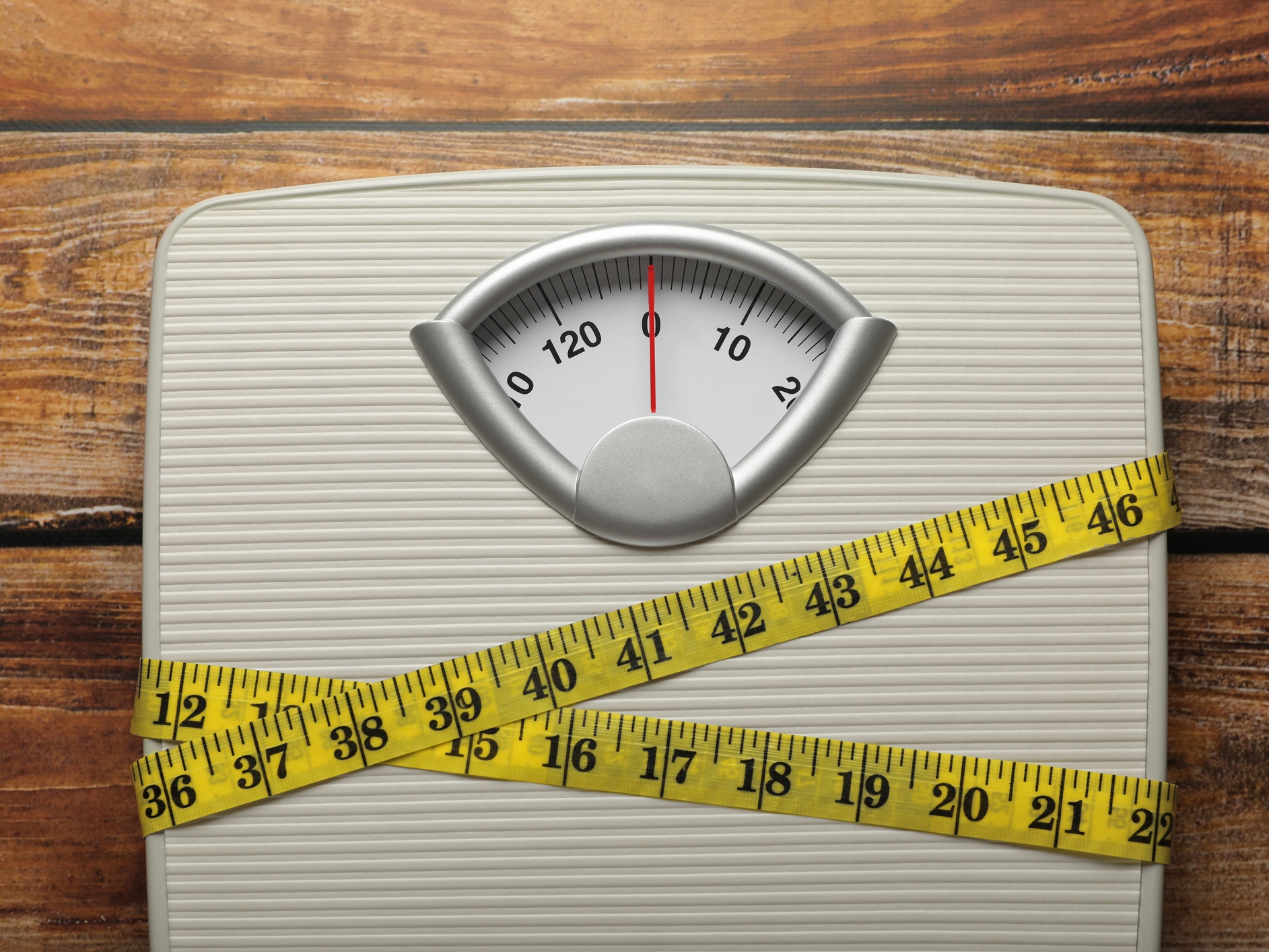 Weigh scales tied with measuring tape on wooden table, top view. Overweight concept
