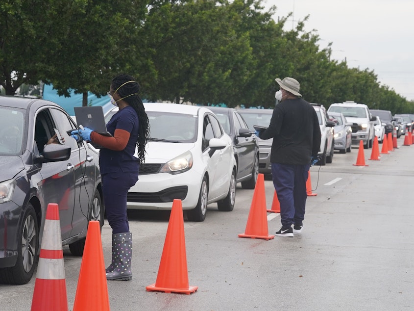 caption: Employees of Nomi Health check in a long line of people seeking COVID-19 tests Tuesday in North Miami, Fla. The omicron variant has unleashed a fresh round of fear and uncertainty for travelers, shoppers and partygoers across the U.S.