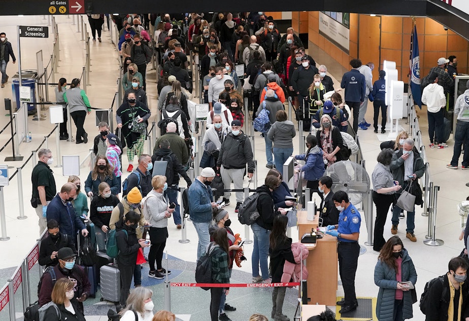 caption: Travelers wear masks as they wait in a line for a TSA security check, Dec. 10, 2021, at Seattle-Tacoma International Airport in Seattle. 
