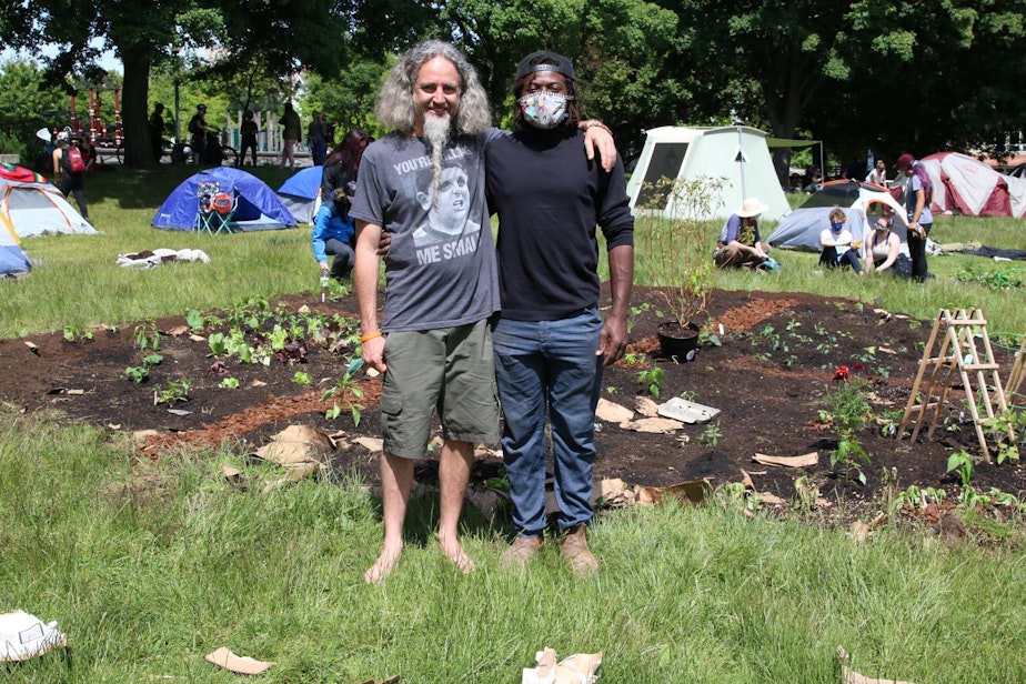 caption: Marcus Henderson (R) came down with a shovel on his bike and started digging. Others donated compost, plants. Water comes from the reservoir fountain behind them.