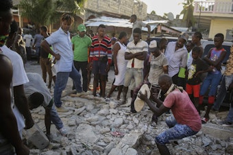 caption: A man digs with a stone through the rubble of a house destroyed by the earthquake in Les Cayes, Haiti, on Sunday.