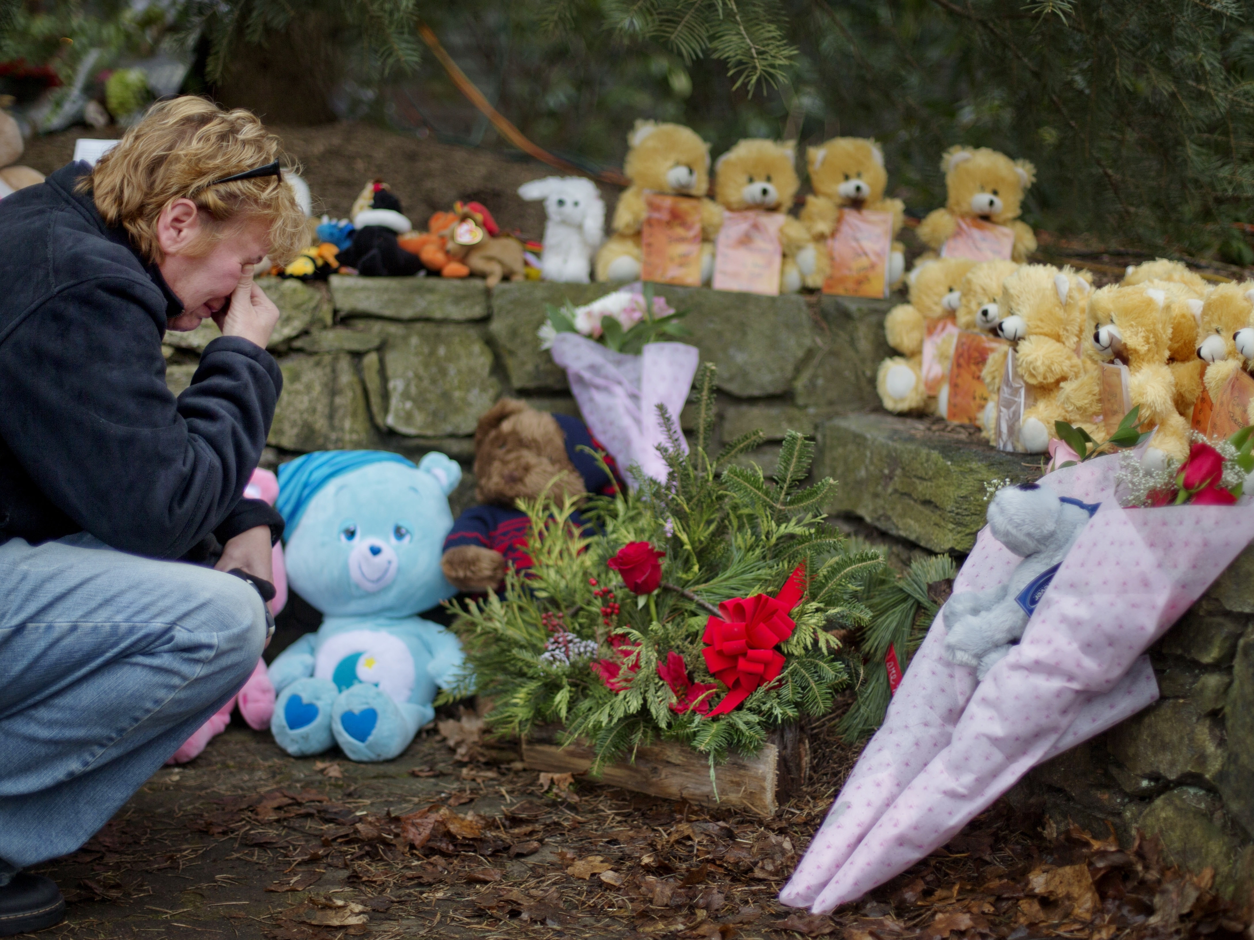 caption: A mourner kneels beside 26 teddy bears, each representing a victim of the Sandy Hook Elementary School shooting, at a sidewalk memorial in 2012 in Newtown, Conn.