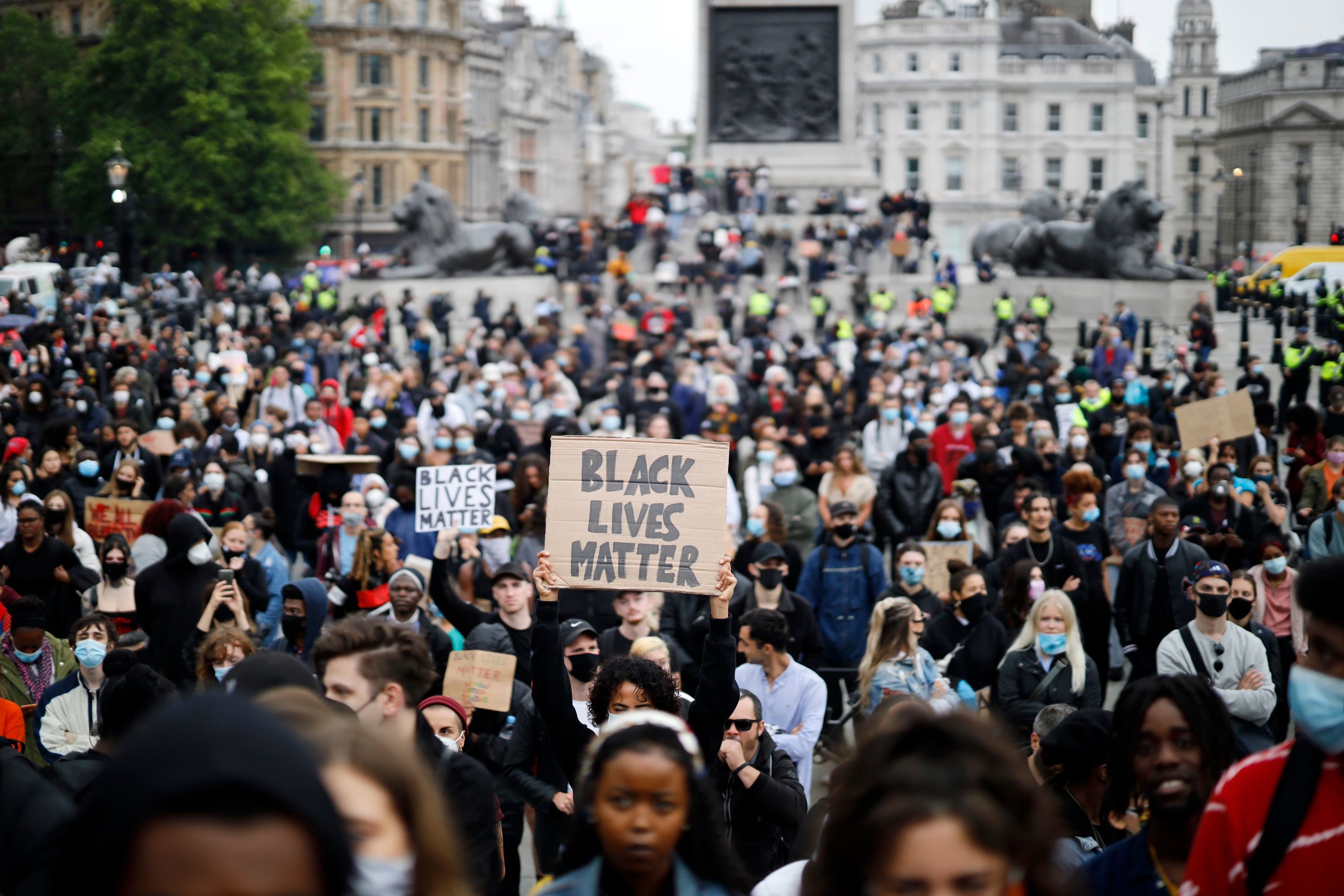 caption: Activists, some wearing face coverings or face masks as a precautionary measure against COVID-19, hold placards as they attend a Black Lives Matter protest in Trafalgar Square in London on June 12, 2020, backdropped by the Houses of Parliament.  (Tolga Akmen/AFP via Getty Images)