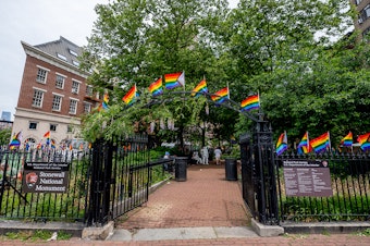 caption: Pride flags decorate the Stonewall National Monument at Christopher Park in front of the Stonewall Inn. Many Pride events this year are more subdued due to pandemic precautions.