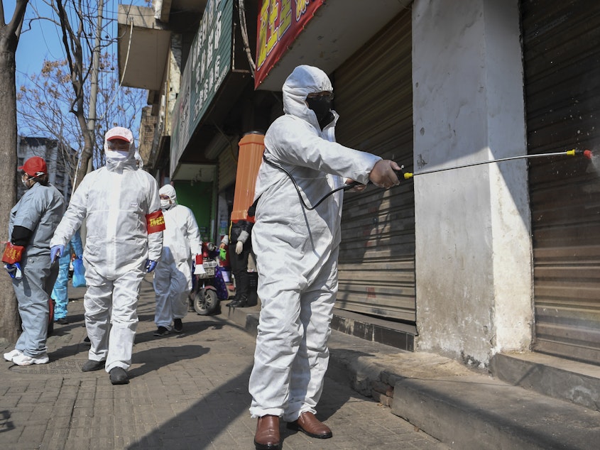 caption: In a photo released by the Xinhua News Agency, workers disinfect closed shop lots following the coronavirus outbreak, in Jiang'an District of Wuhan in central China's Hubei Province, on Monday.