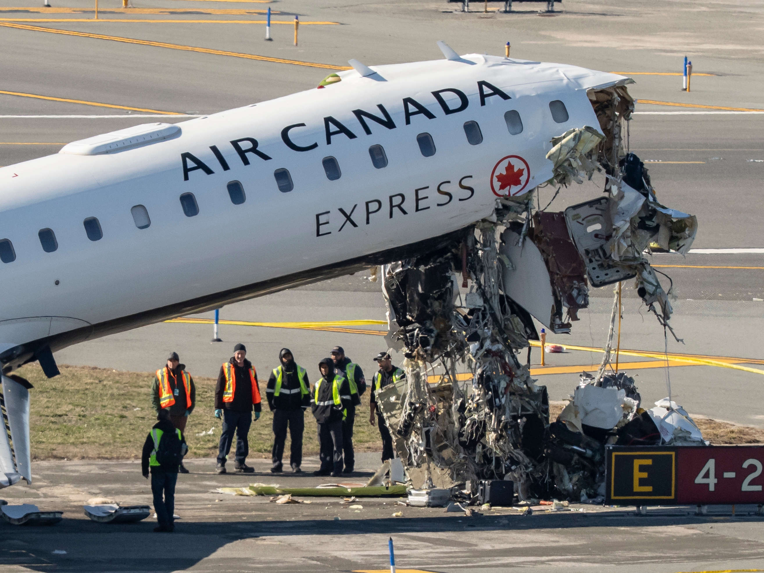 caption: Aircraft maintenance workers inspect the wreckage of an Air Canada Express jet on Tuesday, just off the runway where it collided with a Port Authority fire truck Sunday night at LaGuardia Airport in New York.