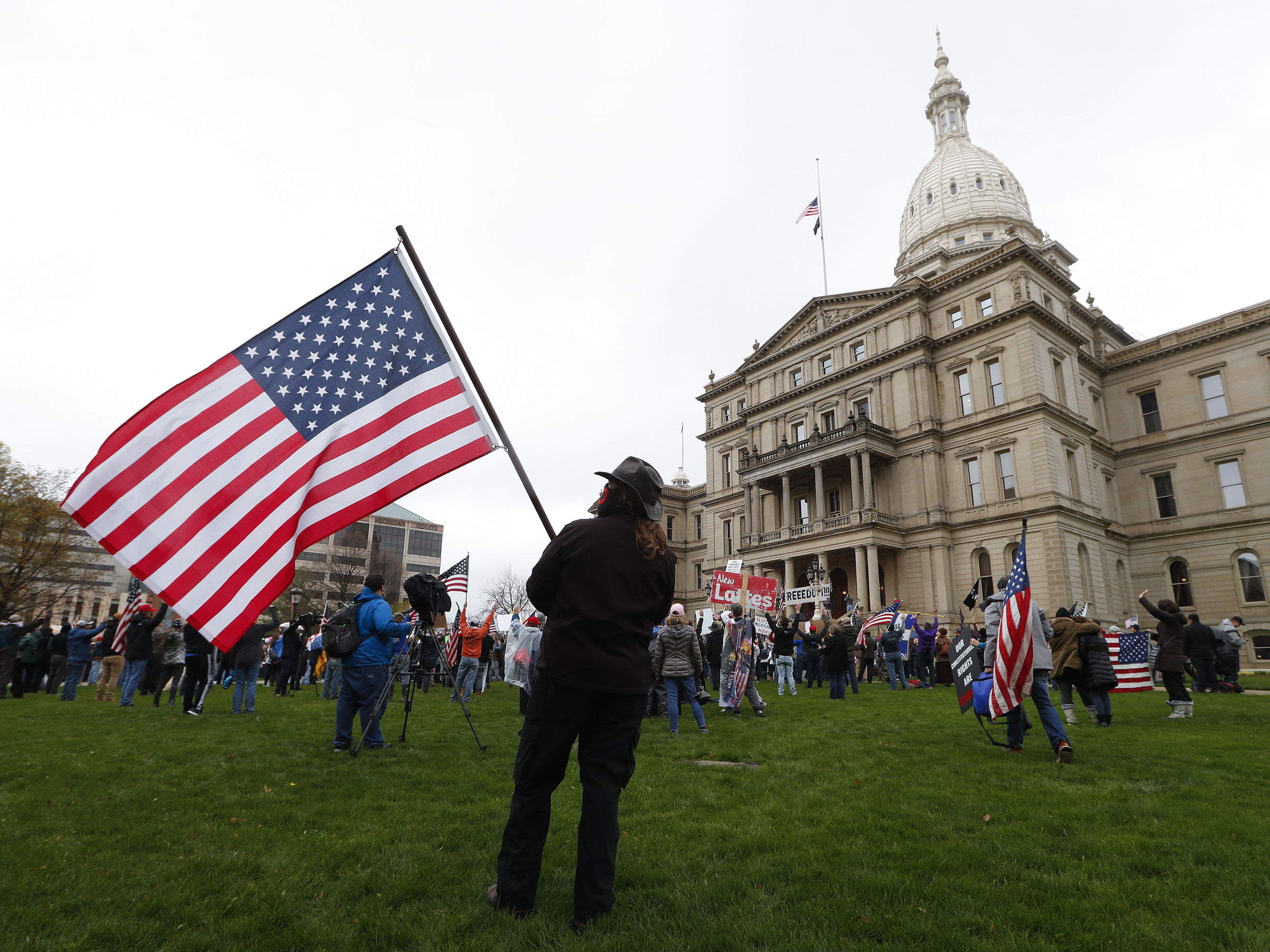 caption: A protester holds an American flag on the lawn of the Michigan Capitol on April 30, 2020. Lawmakers in Shiawassee County are vowing to return $65,000 in bonuses they gave themselves using federal coronavirus relief funds.