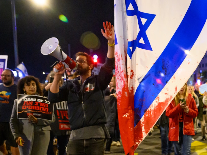 caption: A protester with red paint on his hand marches through the streets after demonstrating outside the Israel Defense Forces headquarters on Friday in Tel Aviv, Israel. Earlier, the IDF had said its forces accidentally killed three hostages being held in Gaza when it mistakenly identified them as potential threats.