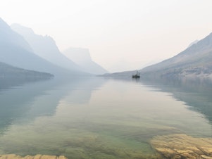 caption: In July wildfire smoke hung over St. Mary Lake in Glacier National Park in Montana  (right). The haze muted the bright views amateur photographer Heather Duchow remembered from and anniversary trip 15 years ago (left).