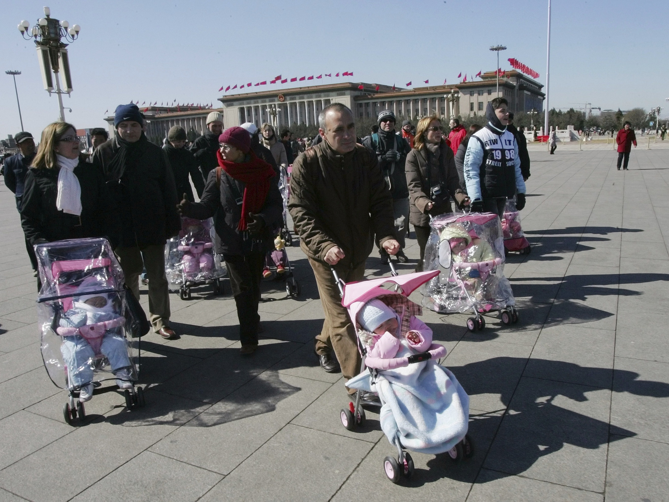 caption: Spanish couples take their newly adopted Chinese children for a walk in Beijing's Tiananmen Square on March 7, 2007. 