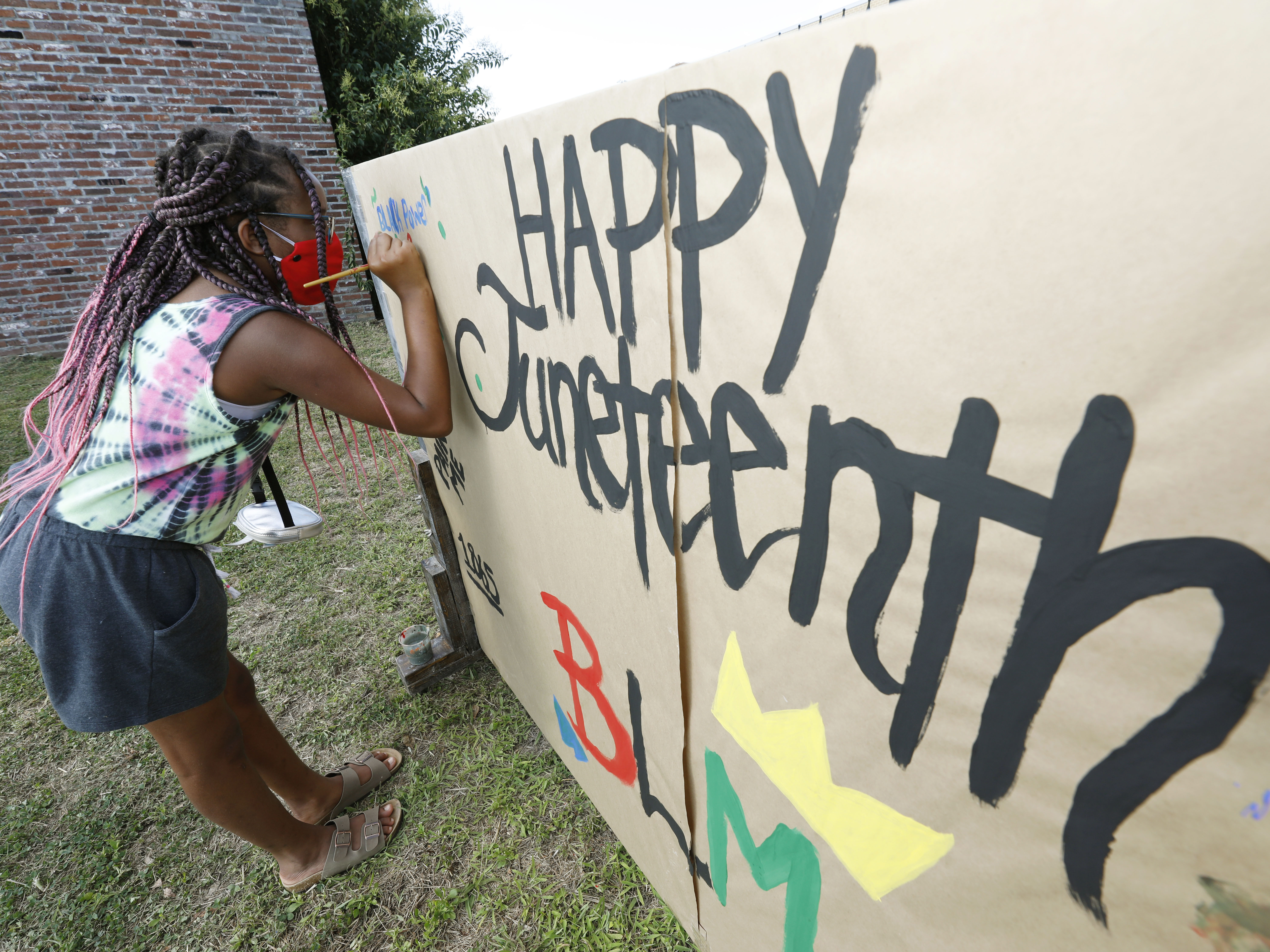 caption: A girl paints on a poster celebrating Juneteenth in downtown Jackson, Miss., on June 19, 2020. Congress has voted to make the day a federal holiday.
