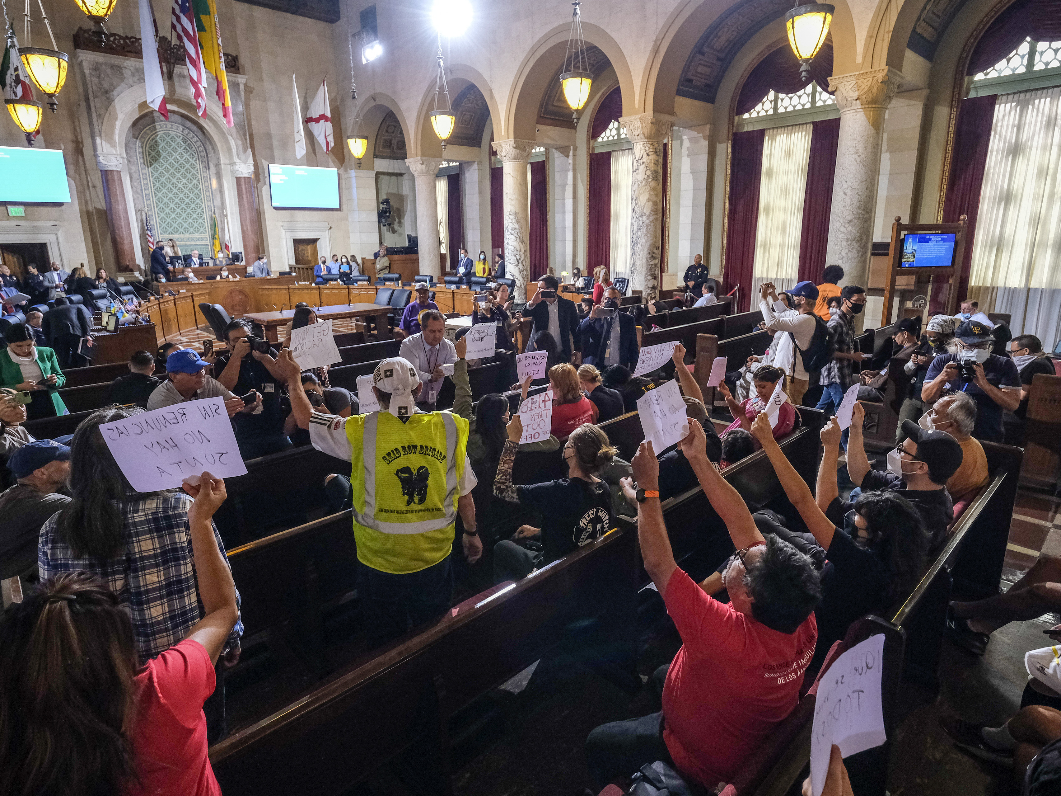 caption: People hold signs and shout slogans as they protest before the cancellation of the Los Angeles City Council meeting Wednesday in Los Angeles.