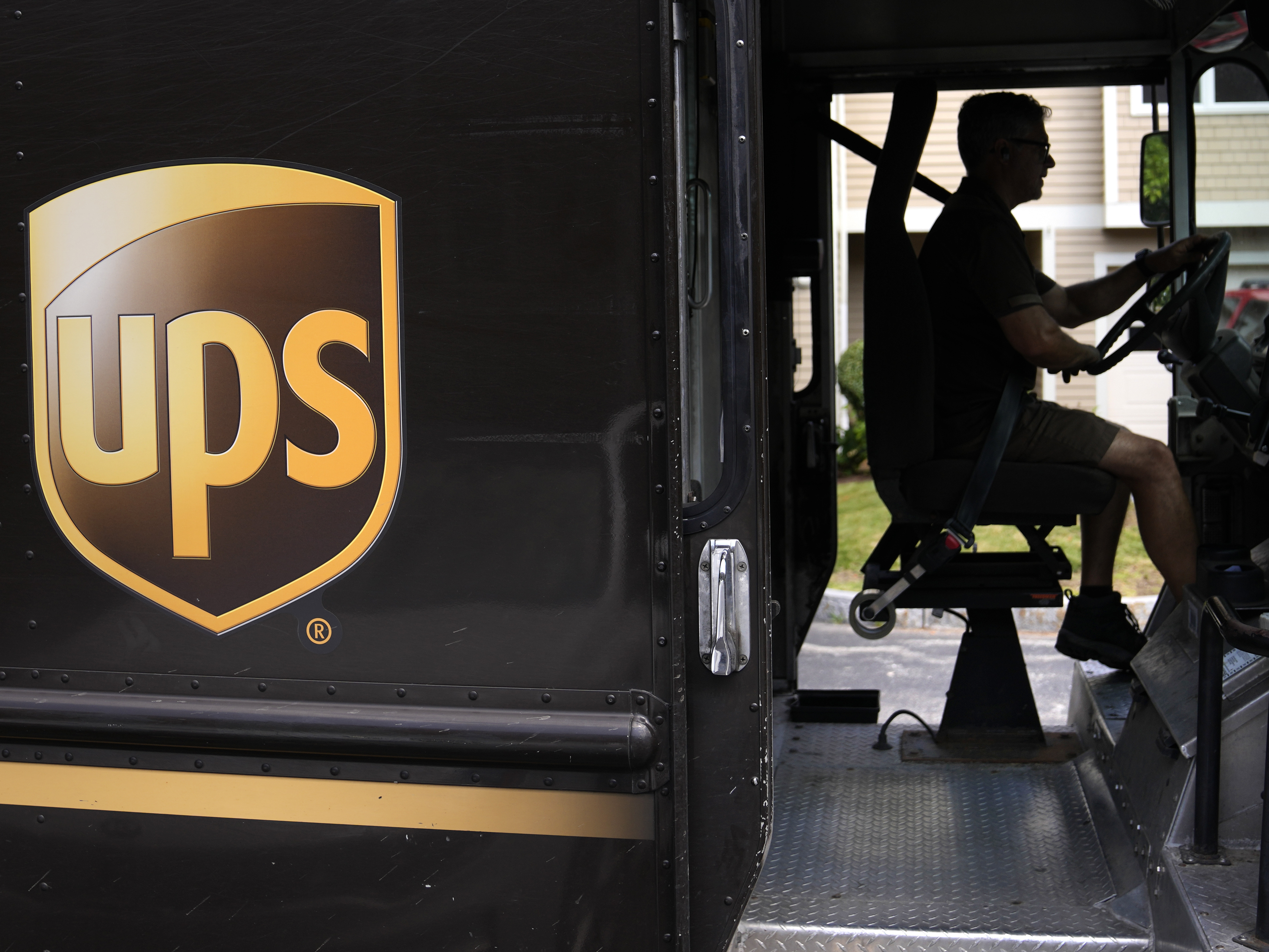 caption: United Parcel Service driver Hudson de Almeida steers through a neighborhood while delivering packages, June 30, 2023, in Haverhill, Mass.