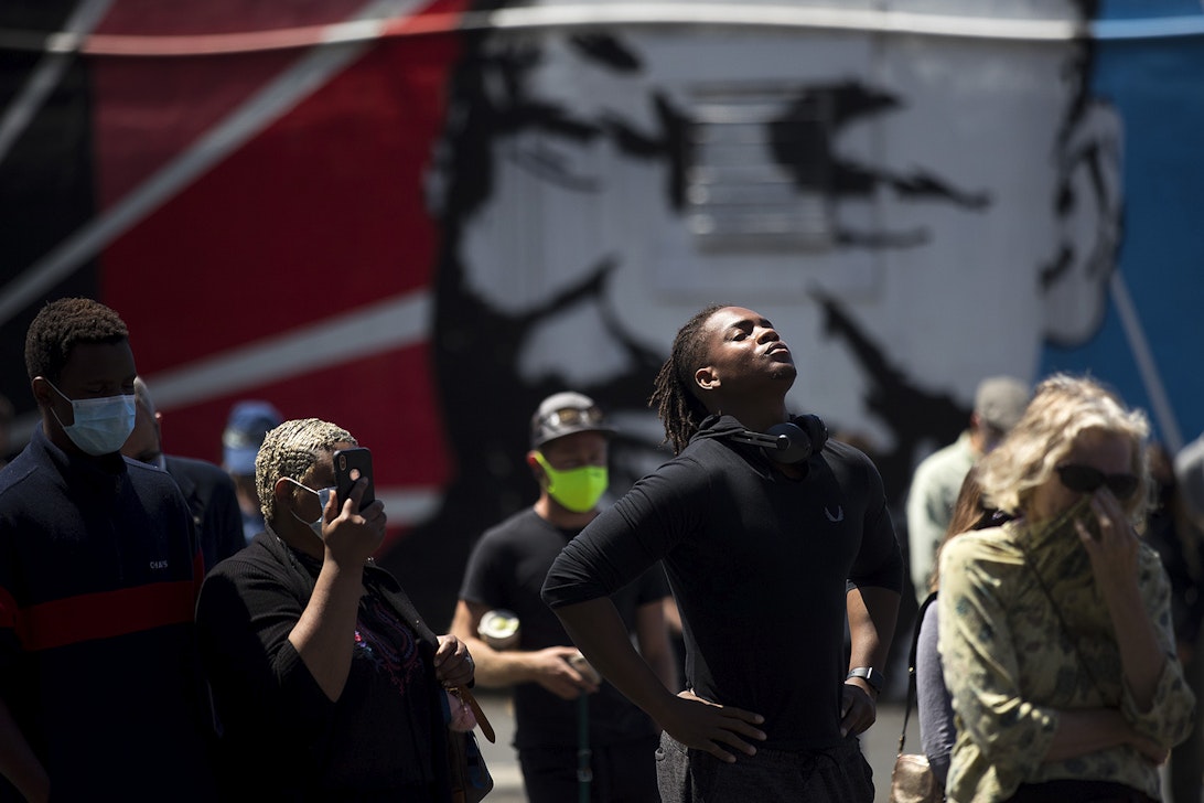 caption: Hanz Jouissance, center, stands in front of a mural of Dr. Martin Luther King Jr. while attending a vigil to recognize the senseless killing of African American men and women outside of the First African Methodist Episcopal Church on Monday, June 1, 2020, in Seattle.