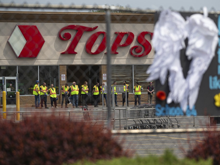 caption: Tops Markets announced Monday that its Buffalo, N.Y. location will reopen on July 15 following the deadly mass shooting in May. Here, investigators stand outside during a moment of silence for the victims of the Buffalo supermarket shooting outside the Tops Friendly Market on Saturday, May 21, 2022.