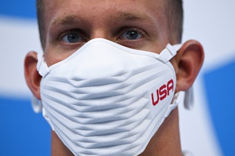 caption: Team USA's Caeleb Dressel wears a USA-branded face covering while waiting to receive his gold medal after the final of the men's 4x100 meter freestyle relay swimming event during the Tokyo Olympics at the Tokyo Aquatics Centre on Monday.