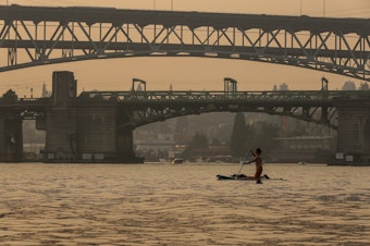 caption: A paddle boarder crosses Portage Bay through heavy smoke from nearby wildfires on Sunday, August 20, 2023, in Seattle.