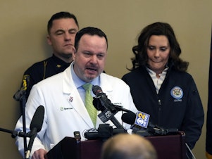 caption: Dr. Denny Martin, the acting chief medical officer at Sparrow Hospital, got emotional while addressing the media on Tuesday following a shooting at Michigan State University. Behind him is Gov. Gretchen Whitmer.