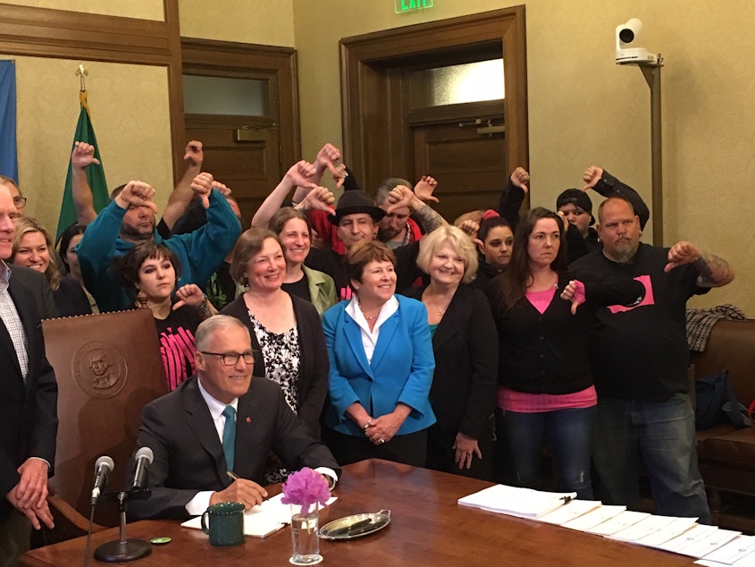 caption: Vape shop owners give the thumbs down sign as Gov. Jay Inslee poses for a photo after signing into law a new tax on vaping liquids.