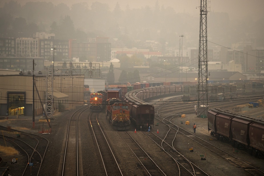 caption: Air quality in Seattle has turned hazardous according to the state Department of Ecology, as wildfire smoke from California and Oregon continues to settle in the area. Here, a worker walks through Balmer Yard on Saturday, September 12, 2020, in Seattle. 
