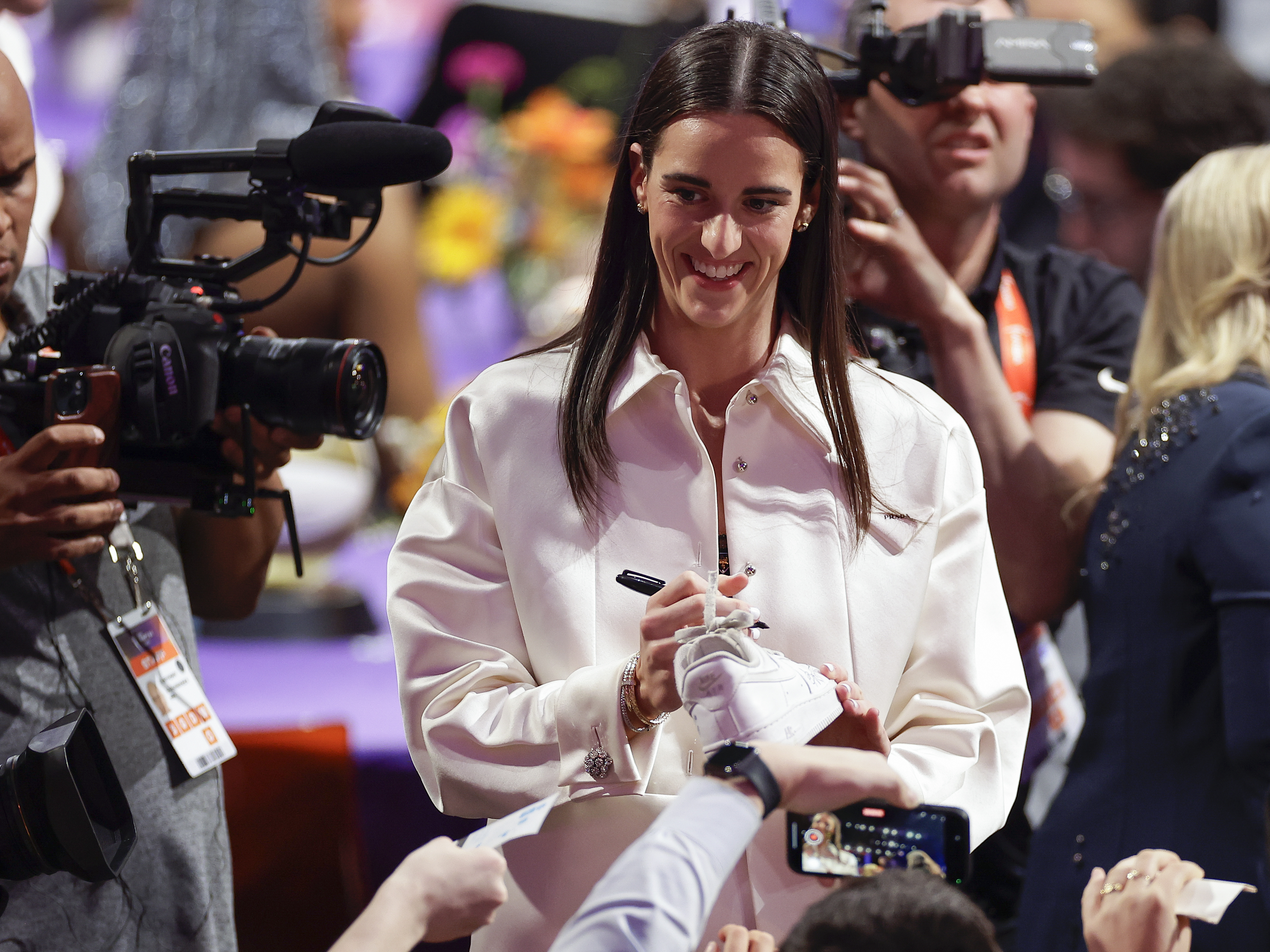 caption: Caitlin Clark, pictured autographing sneakers before the WNBA draft last Monday, is helping drive demand for the league's ticket sales and TV coverage.