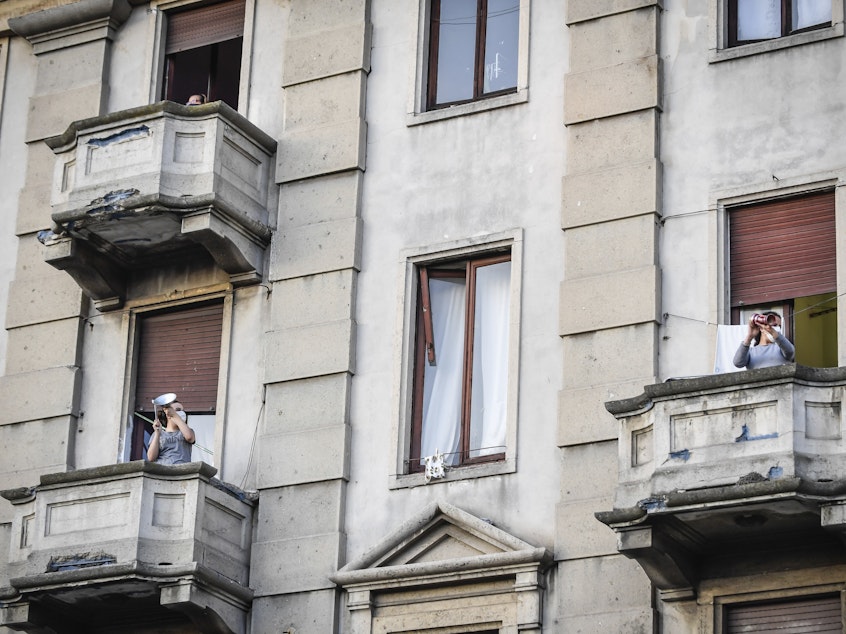 caption: People lean out of their homes' balconies to play and sing during a flash mob in Milan, Italy, Friday, March 13, 2020. Italians have not been able to leave their homes since March 9, when the government locked the country down to combat the spread of coronavirus. (Claudio Furlan/AP)