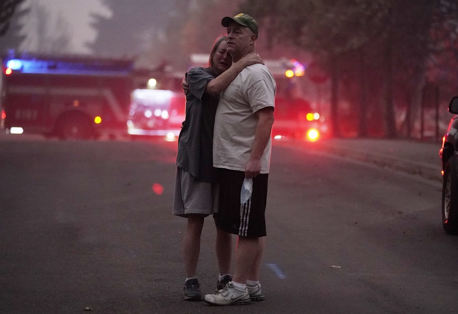 caption: A couple embrace Thursday while touring an area devastated by the Almeda Fire in Phoenix, Ore.