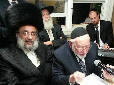 caption: The late Hasidic composer Ben Zion Shenker sings, wearing a yarmulke and holding a mic, at a male-only sing along known as a k<em>umzits </em>that took place in an Orthodox neighborhood in Brooklyn.