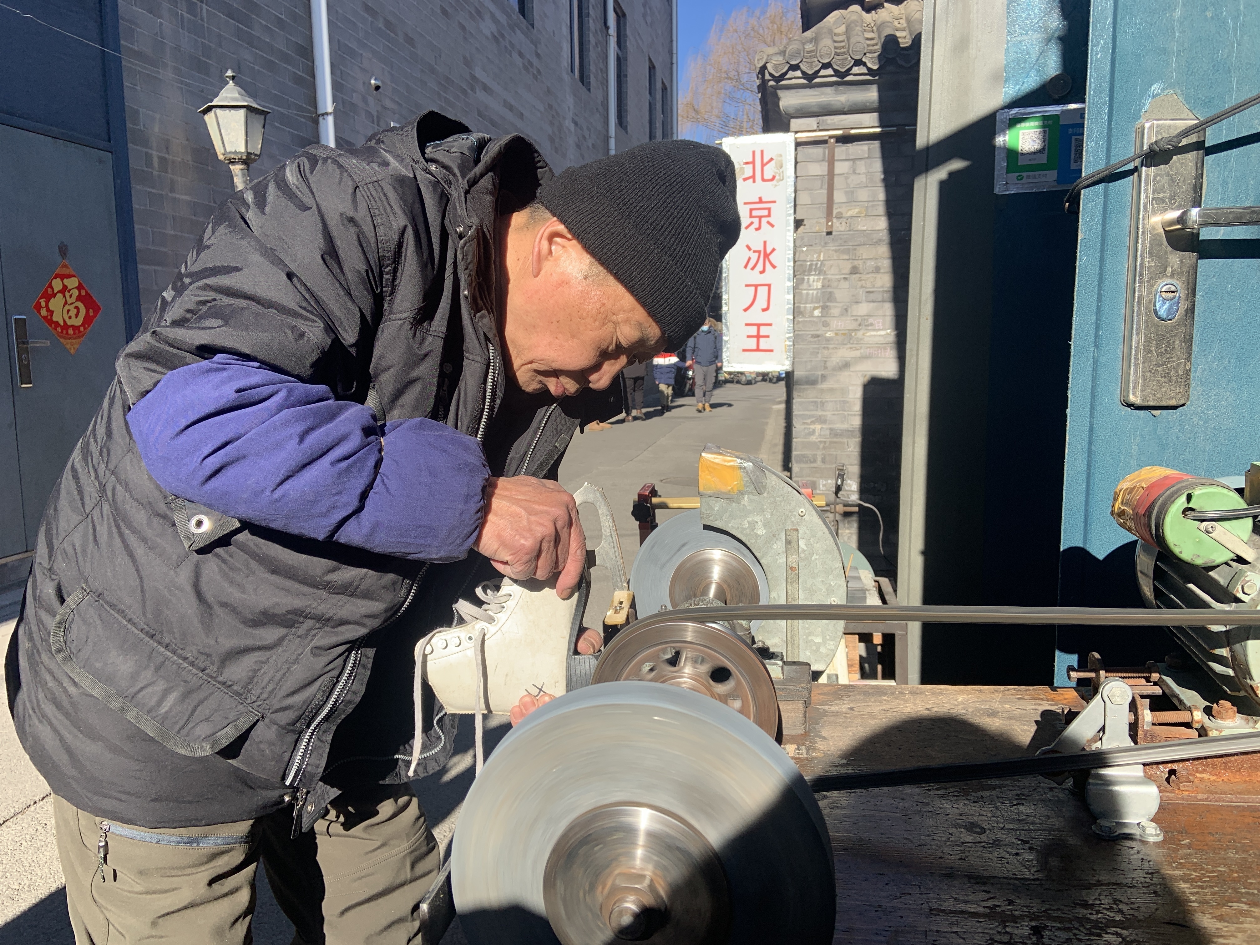 caption: Wang Jianzhi, shown here burnishing a pair of ice skates, runs a famous blade sharpening shop in Beijing near Houhai, a frozen lake popular among outdoor skaters.