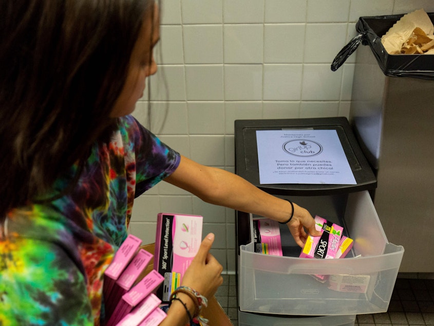 caption: A student stocks a school bathroom with free pads and tampons to push for menstrual equity, at Justice High School in Falls Church, Va., in 2019.