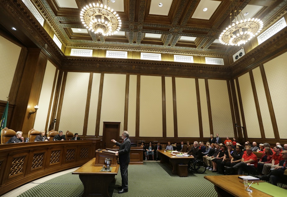 caption: Alan Copsey, center, a deputy attorney general for the state of Washington, speaks during a hearing before the Washington State Supreme Court regarding a lawsuit against the state over education funding, Wednesday, Sept. 7, 2016, in Olympia, Wash.
