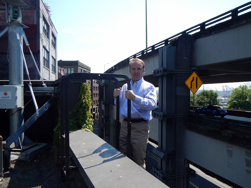 caption: Architect Brian Runberg climbing onto the roof of the building he owns, with a building motion detector above him and the Alaskan Way Viaduct directly behind him.